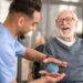 Patient, der seine Hand mit einem stacheligen Massageball massiert bekommt durch eine Pflegekraft
