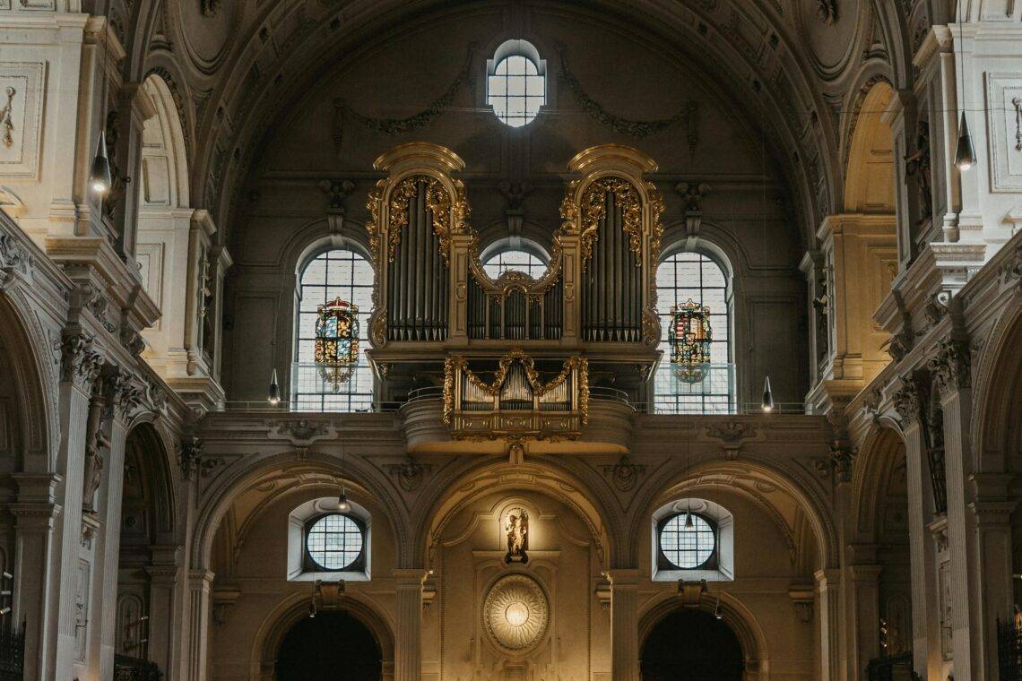 Innenansicht einer Münchner Kirche, die sich für Trauerfeiern eignet, mit imposanter Orgel und Buntglasfenstern, die eine würdevolle und friedvolle Atmosphäre ausstrahlen