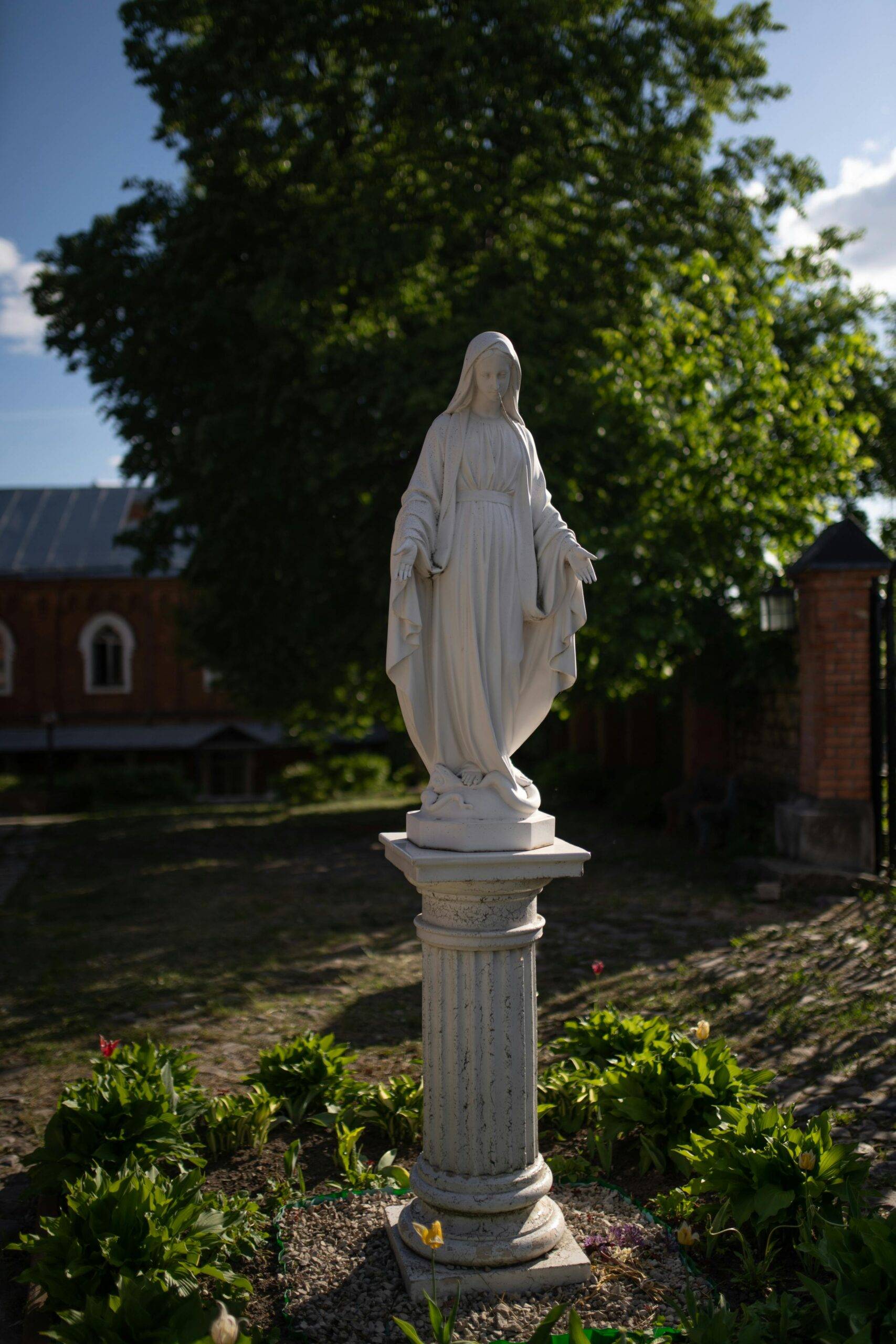 Weiße Statue der Jungfrau Maria auf einem Sockel, umgeben von sanftem Grün, in einem ruhigen Garten, der als Ort der Kontemplation und des Gedenkens für Trauerfeiern in München dient