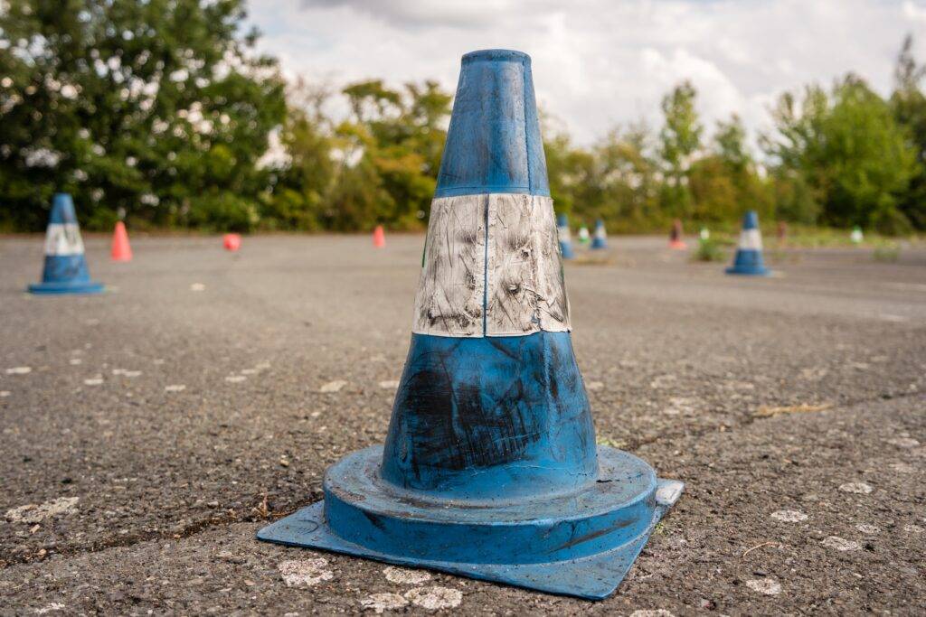 Nahaufnahme eines blauen Verkehrskegels auf einem Asphaltplatz, umgeben von mehreren anderen Kegeln in verschiedenen Farben