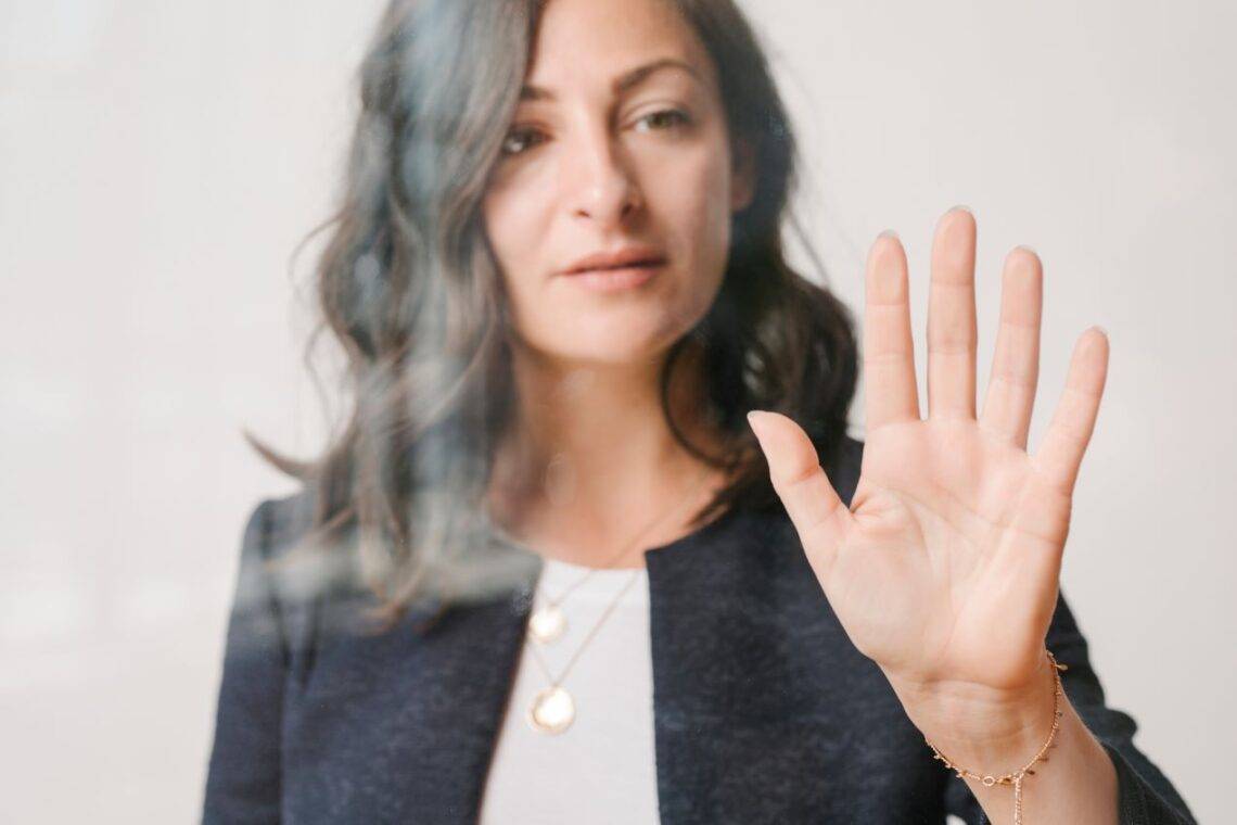 Frau mit schwarzem Blazer und Schmuck berührt eine durchsichtige Glasfläche, symbolisiert moderne transparente Technologie