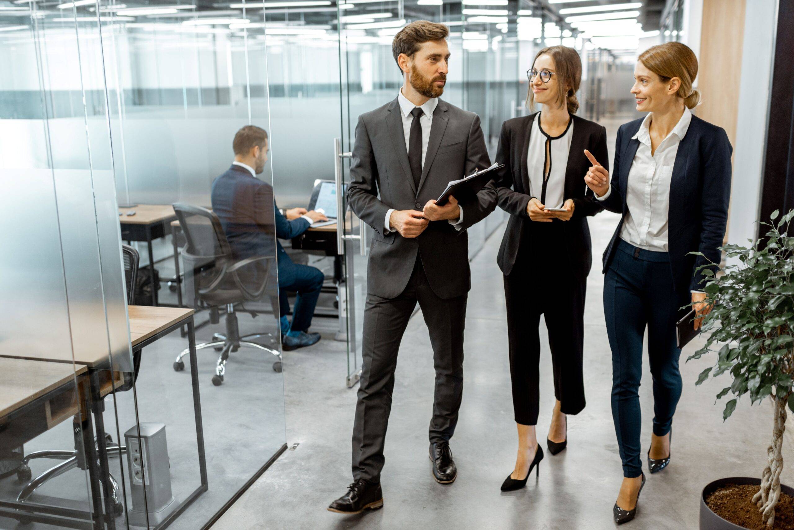 Business-Team geht durch modernes Büro mit Glaswänden – Wirkung professioneller Gebäudereinigung auf potenzielle Kunden und Geschäftspartner