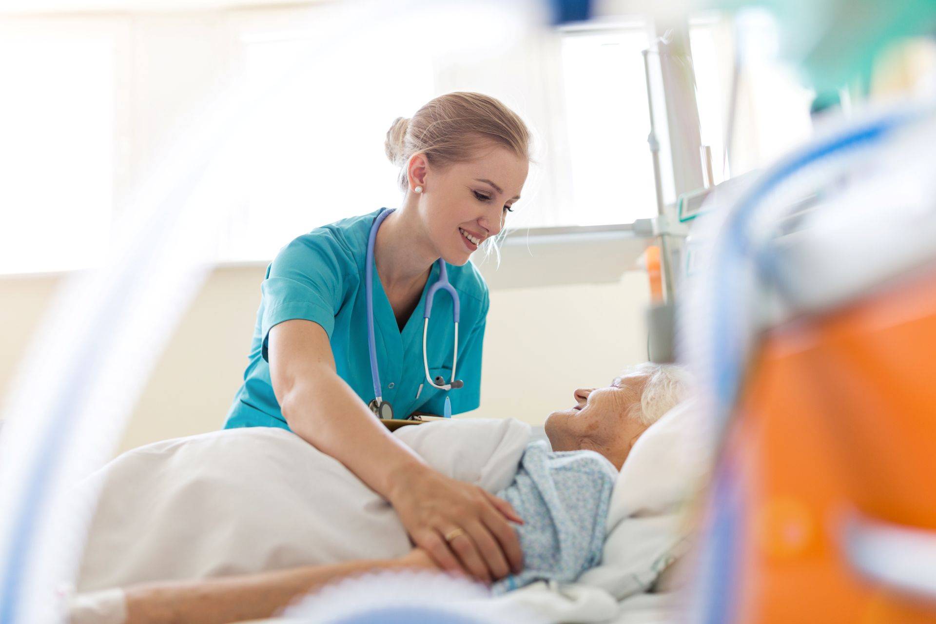 Pflegekraft spricht freundlich mit Seniorin im Krankenbett – persönliche Zuwendung im Pflegealltag