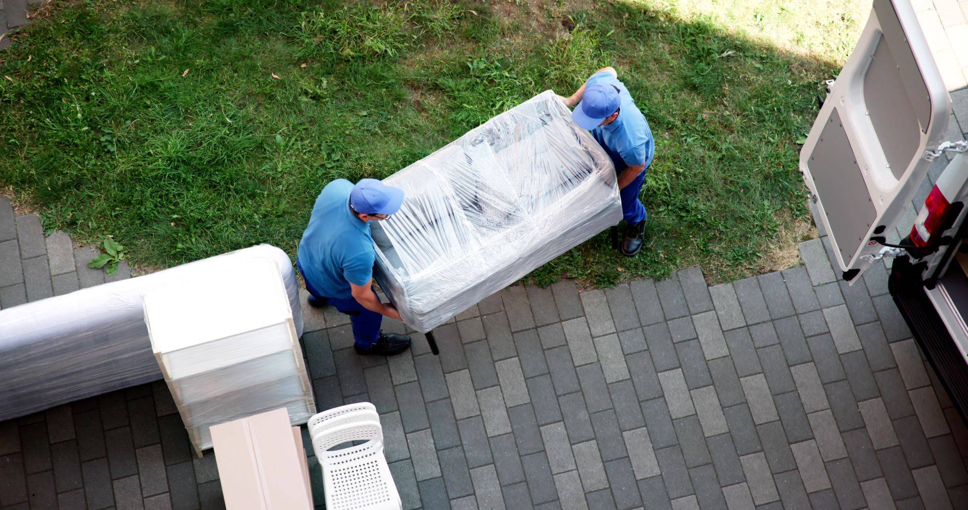 zwei Umzugshelfer tragen ein verpacktes Moebelstueck in ein Transportfahrzeug, professionelle Entruempelung Lippstadt beim Ausraeumen einer Wohnung